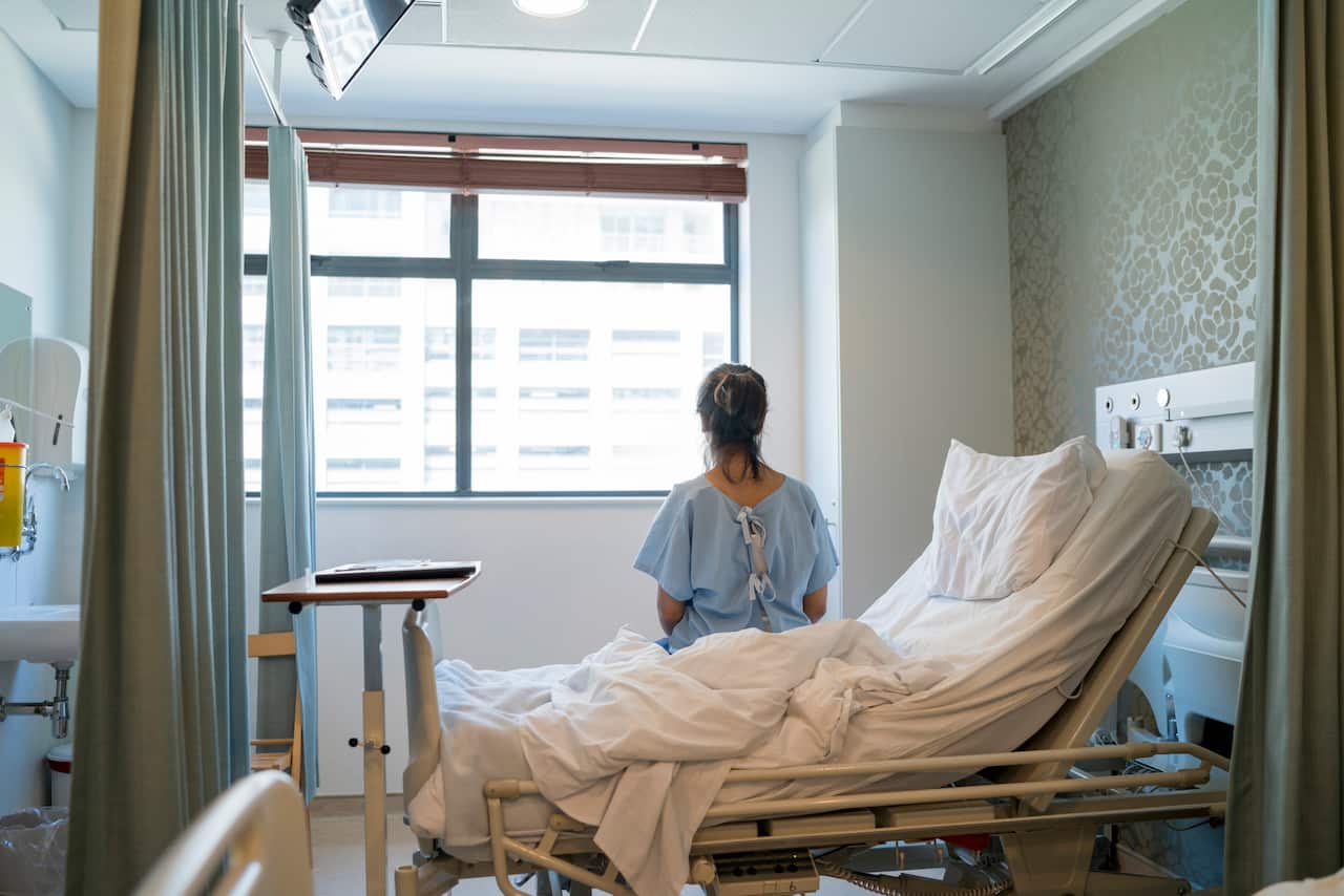 A female patient sitting on a hospital bed with her back towards the camera.