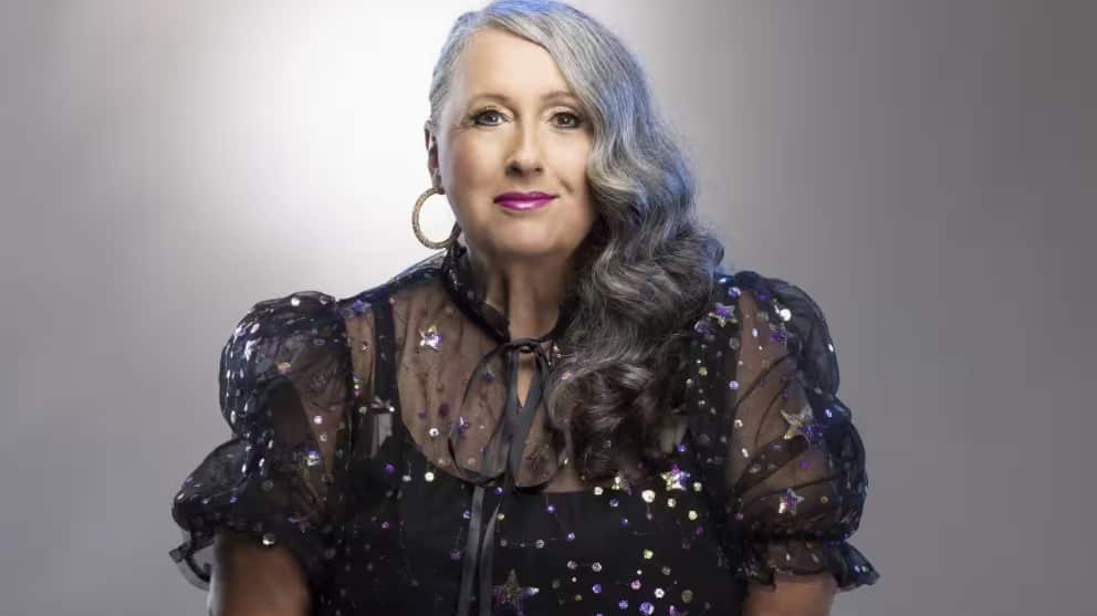 A woman in a black sparkly outfit smiles slightly at the camera.