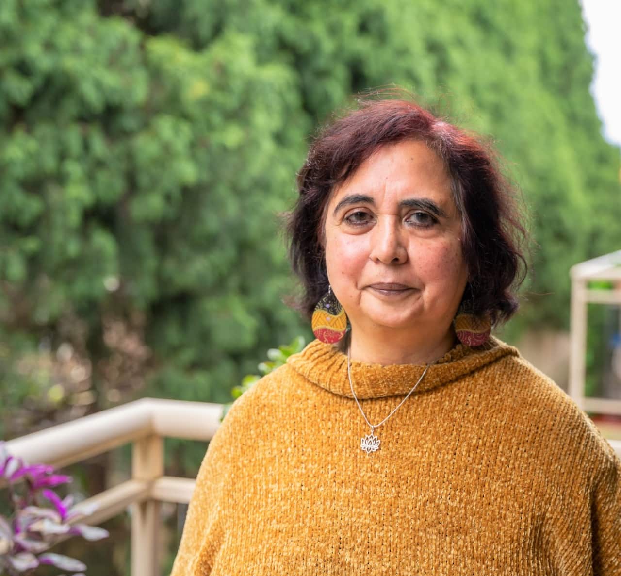 A woman in a yellow jumper stands on a balcony above a garden.