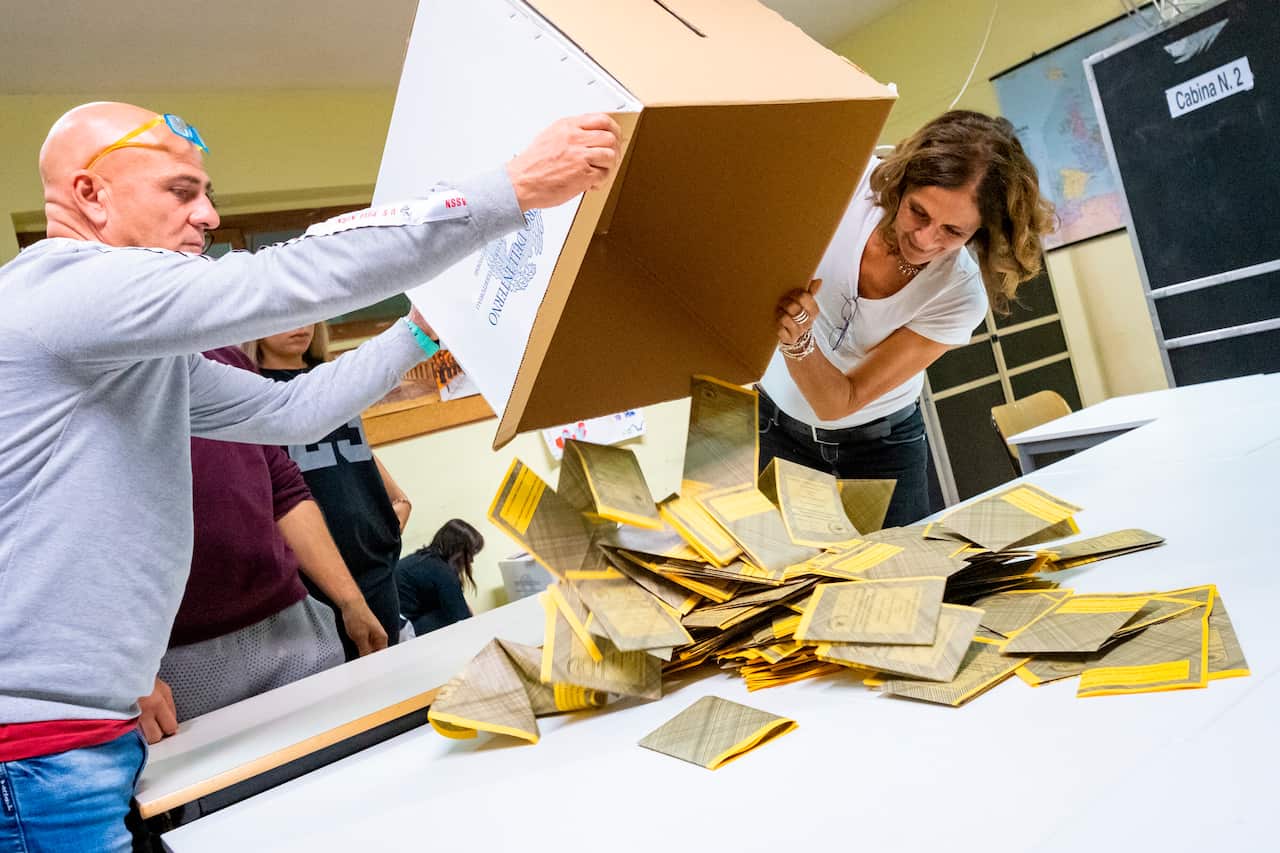 Two people pour a box of ballot papers on a table