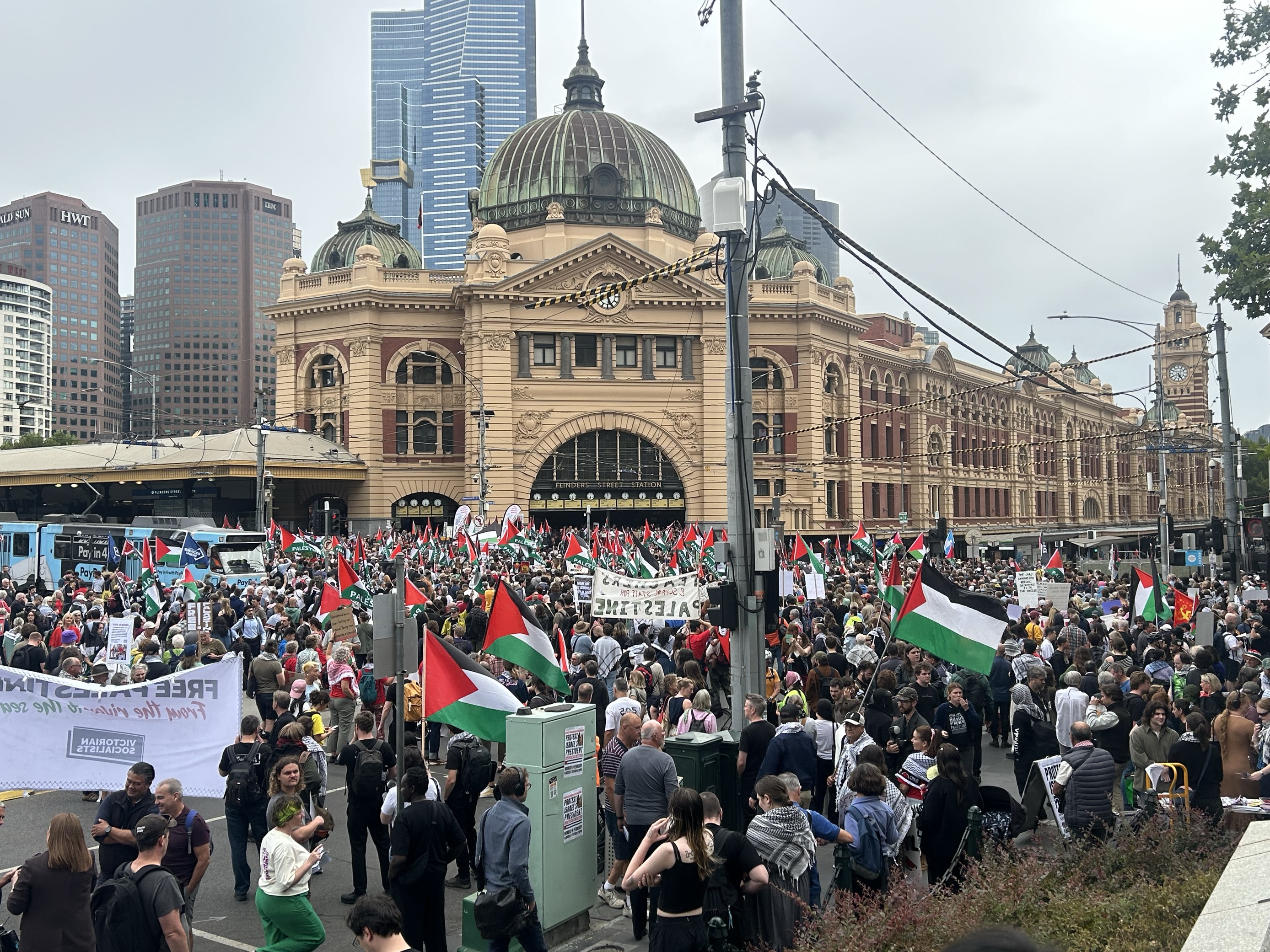 Hundreds of protesters waving Palestinian flags outside a train station in a city 