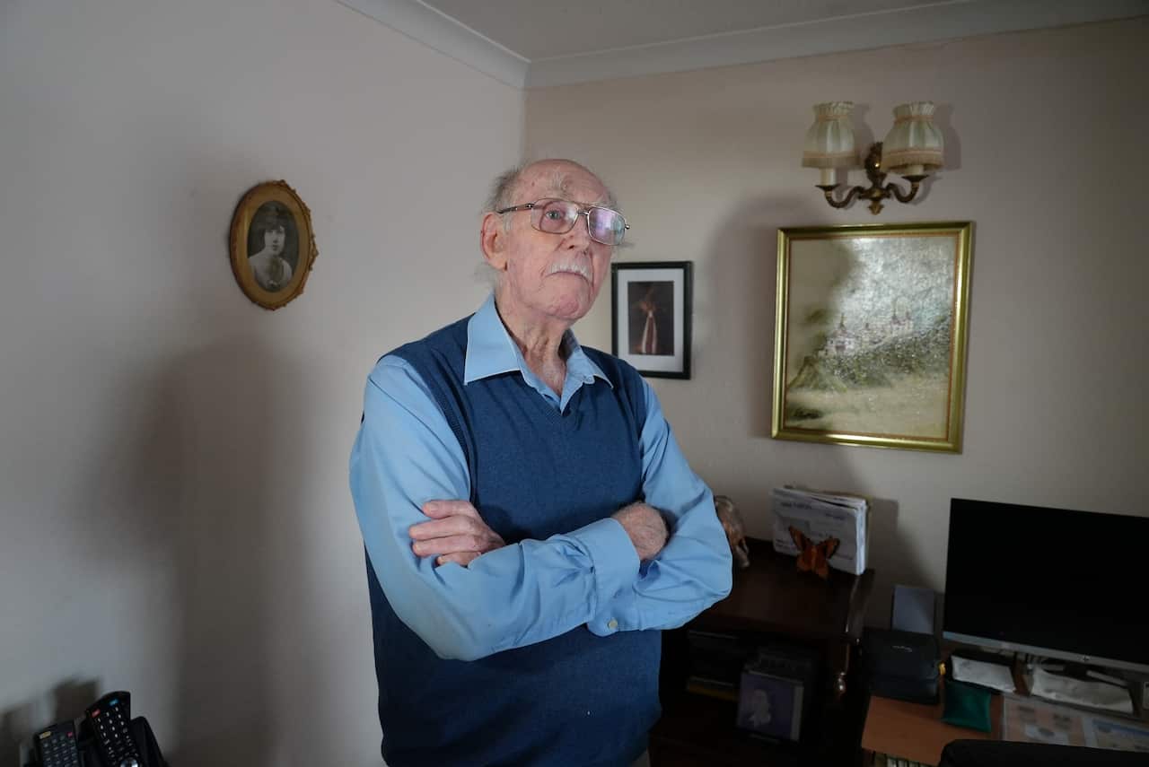 92-year-old Maurice Routhan stands in front of a photo of the Lardil Headdress. 
