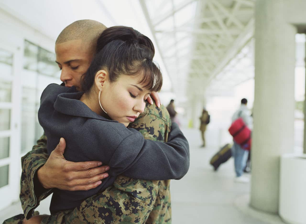 Young couple embracing in airport, man in military uniform