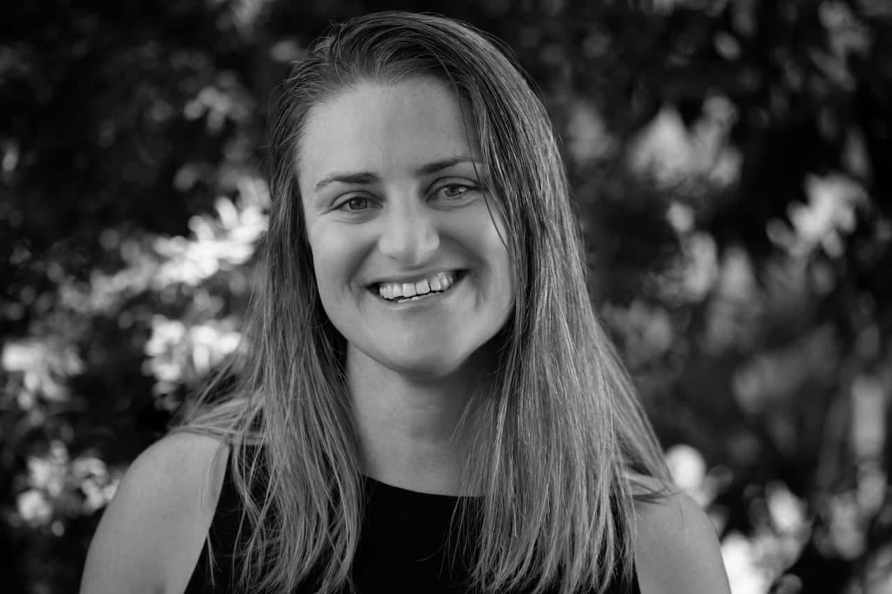 A black-and-white image of a woman with long hair smiling in front of tree leaves
