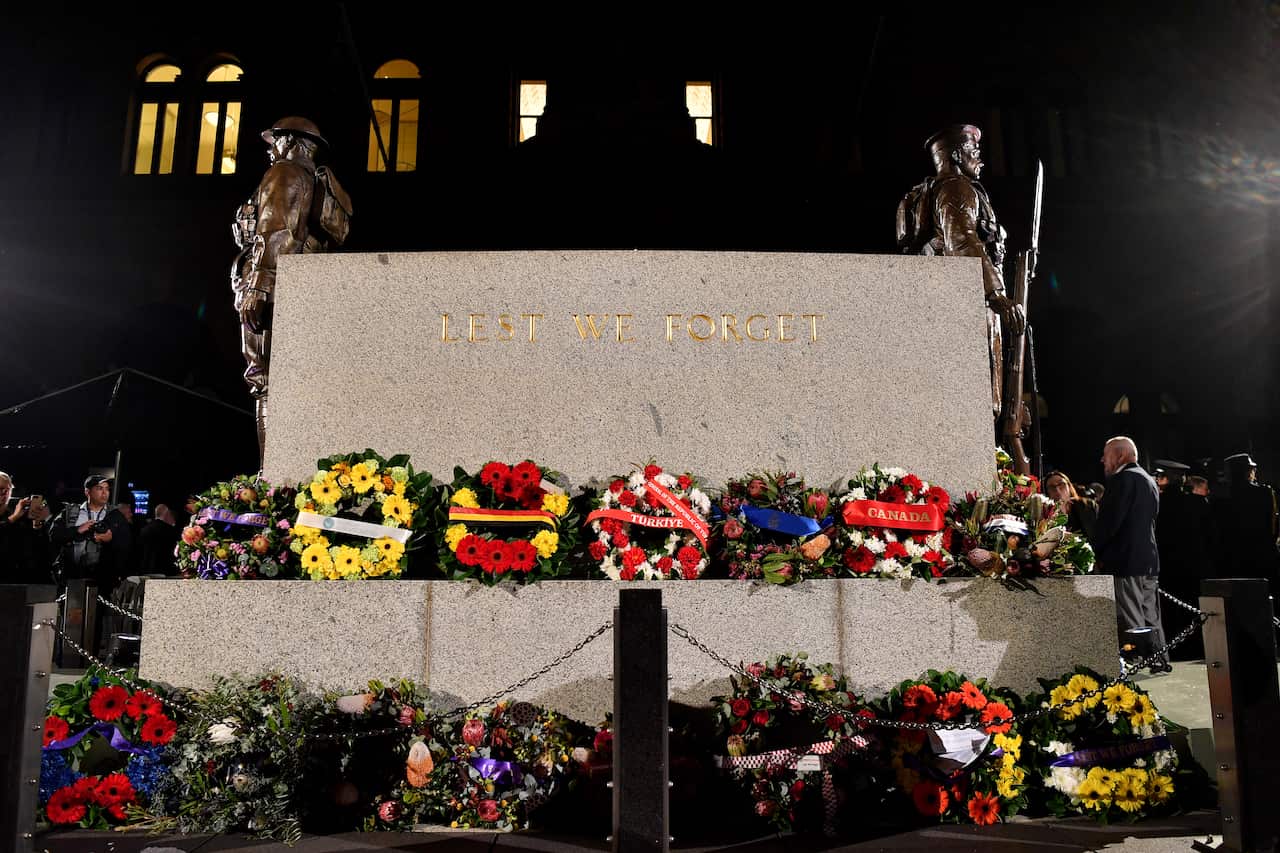 Wreaths placed around and on a large oblong marble monument. The words Lest We Forget are inscribed on the monument in gold lettering.