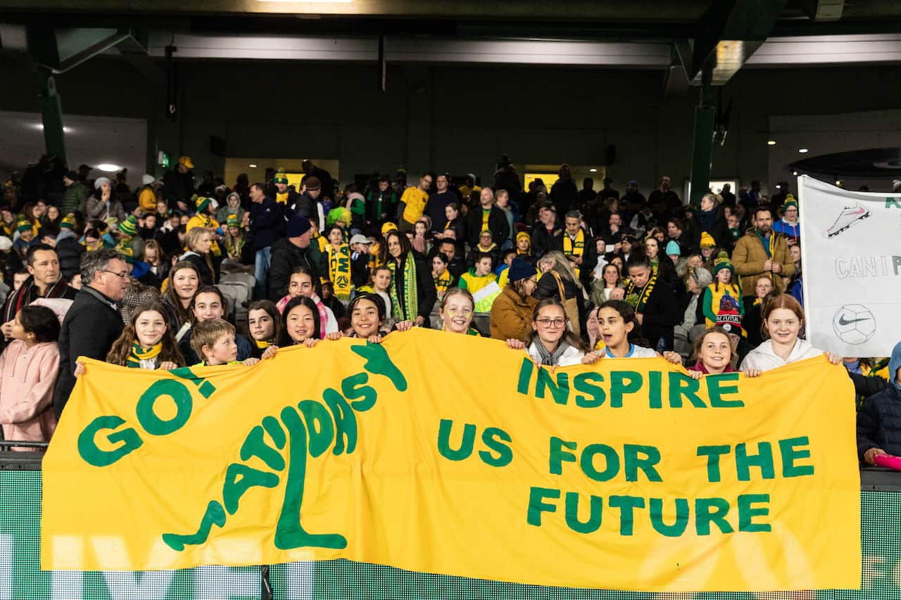 Football fans hold up a yellow banner that reads "Go Matildas! Inspire us for the future."