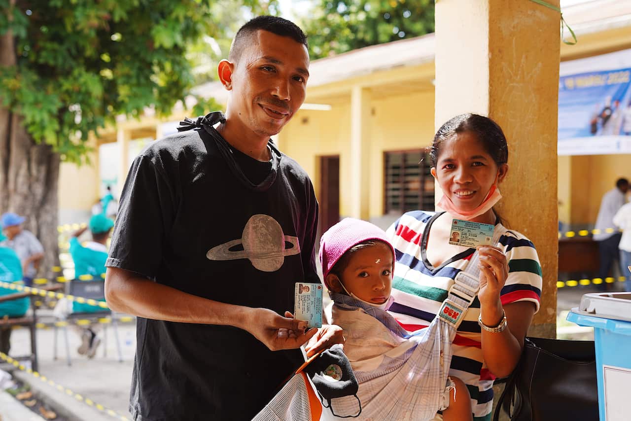 Two voters and a baby pose outside a polling booth in Timor-Leste.