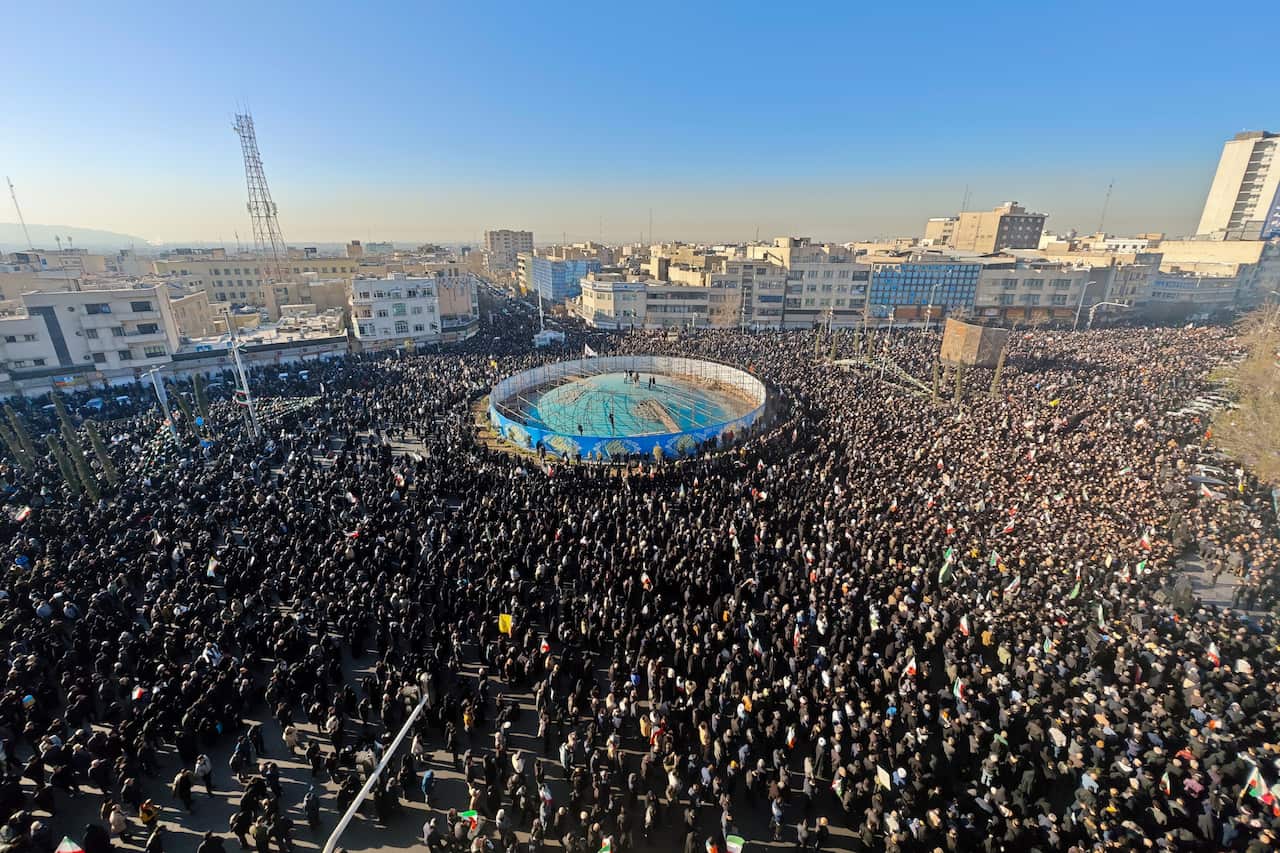 A vast crowd of people gathered in a large city square around a circular blue structure under a clear sky.