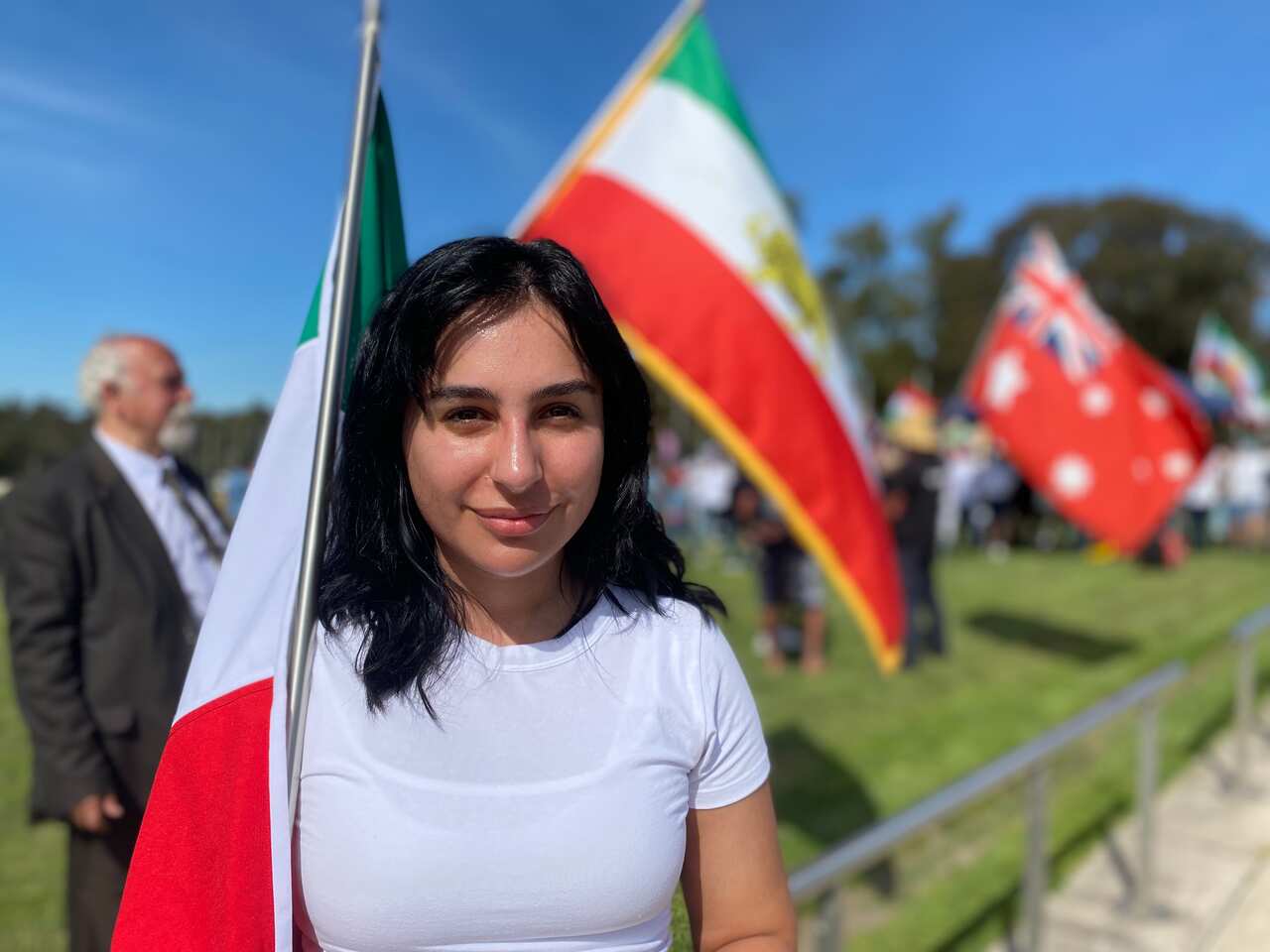 A woman wearing a white t-shirt and holding an Iranian flag outside
