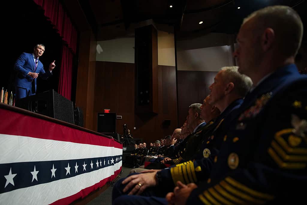 A man on stage in a blue suit addresses a gathering of military commanders in the US.