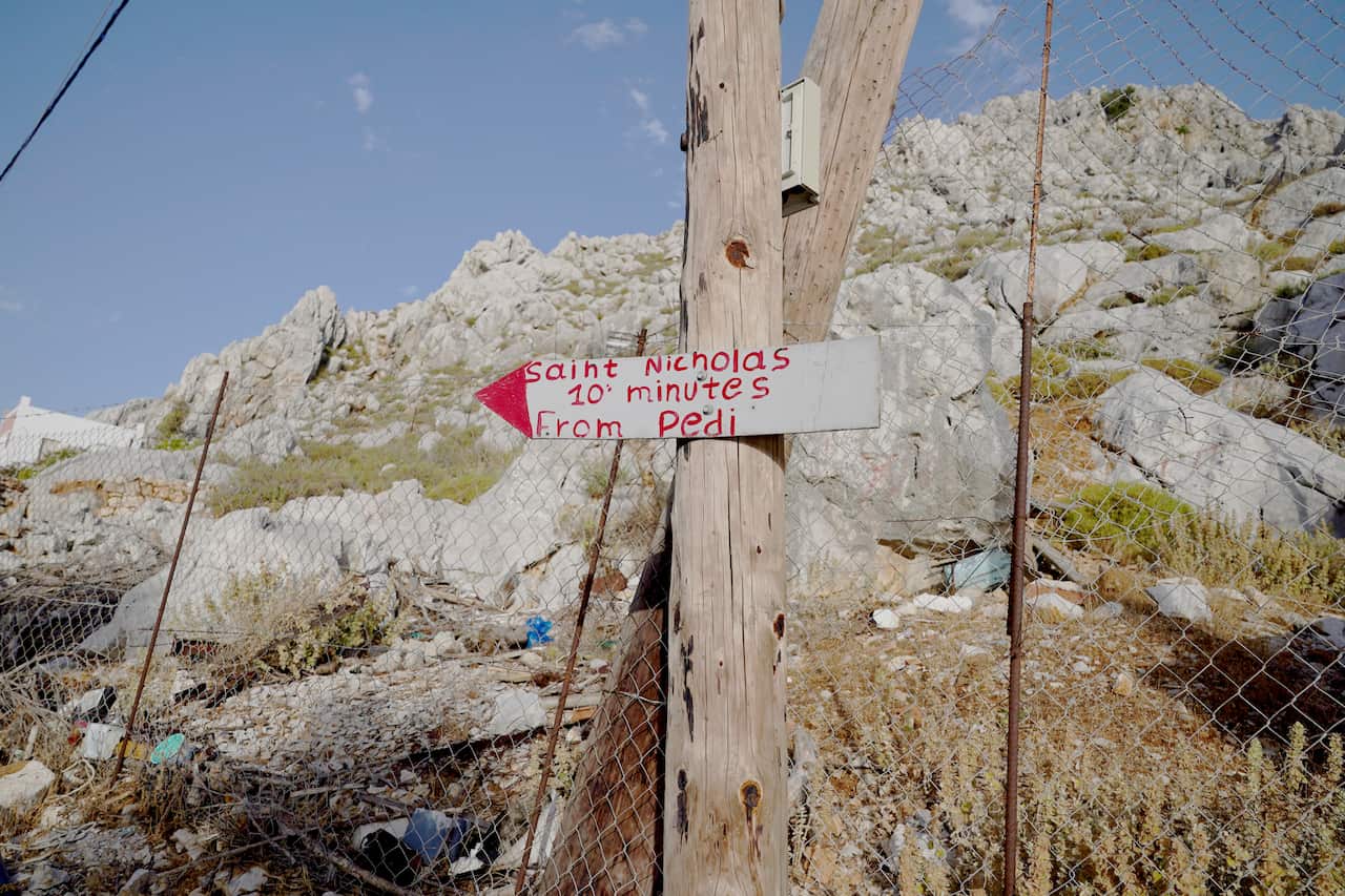 A sign in front of a hill that says "Saint Nicholas 10 minutes from Pedi"