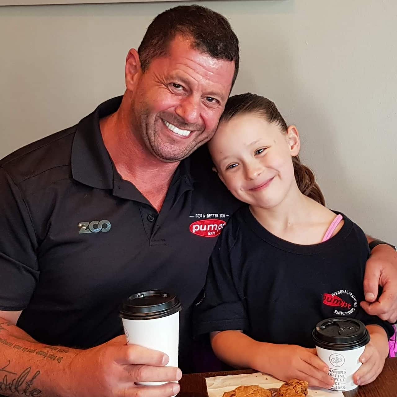 A man hugs his daughter as they hold takeaway cups of coffee.