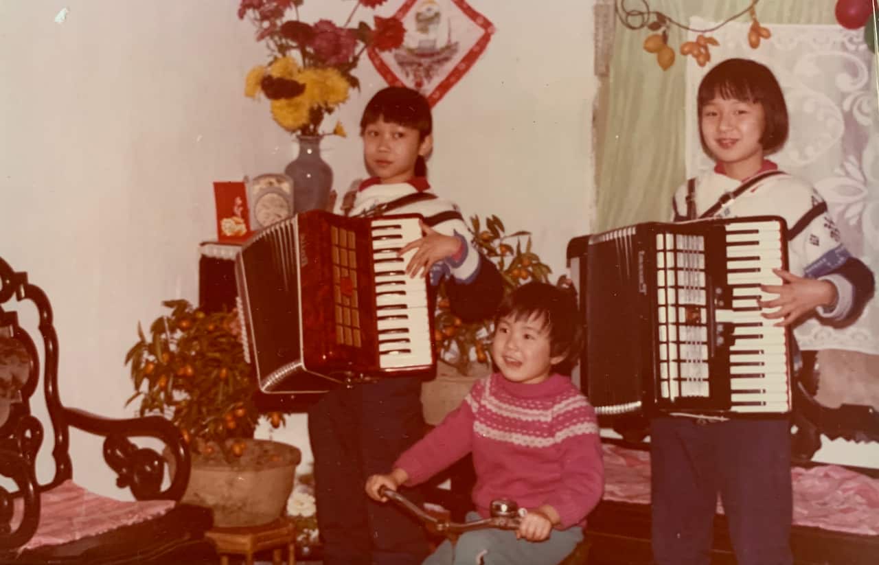 Three young girls, two standing and one sitting in the middle, play musical instruments.
