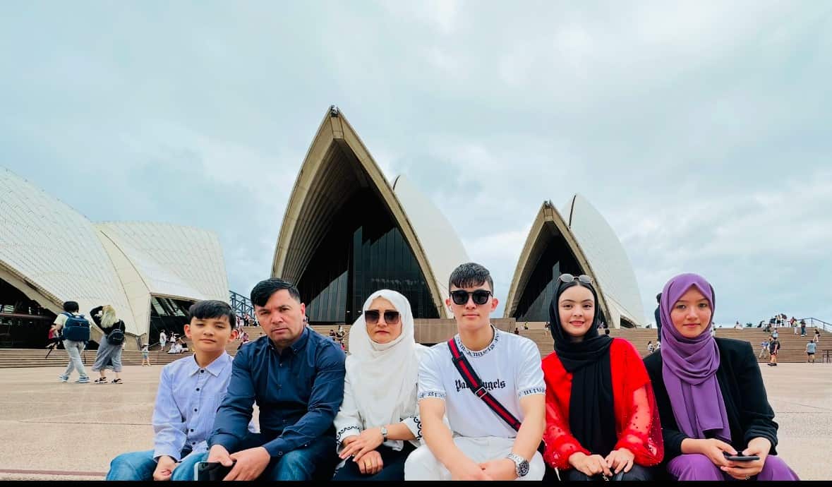 A group of people sit in front of the Sydney Opera House