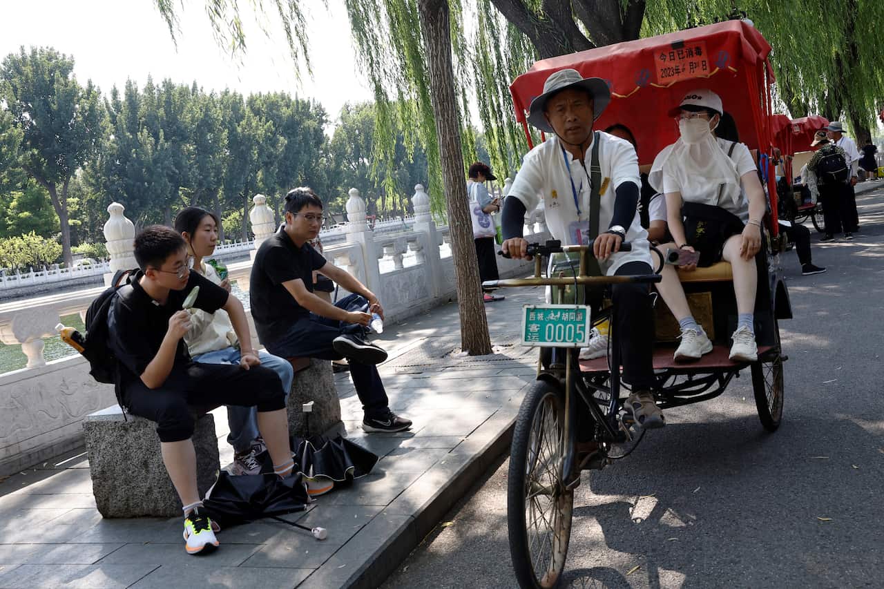 People eat ice creams as a tricycle carrying tourists passes by amid a yellow alert for heatwave, in Beijing,