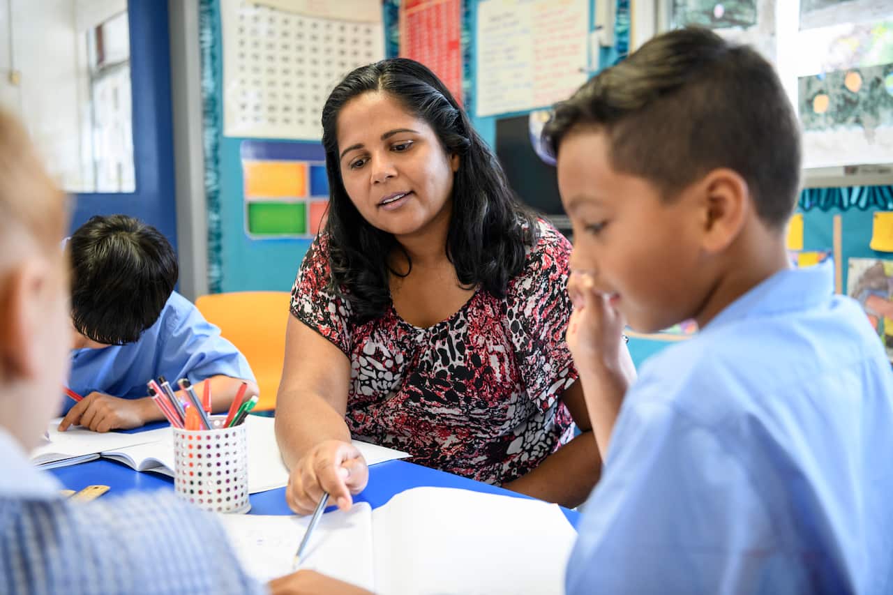 Aboriginal primary school teacher helping young boy in the classroom