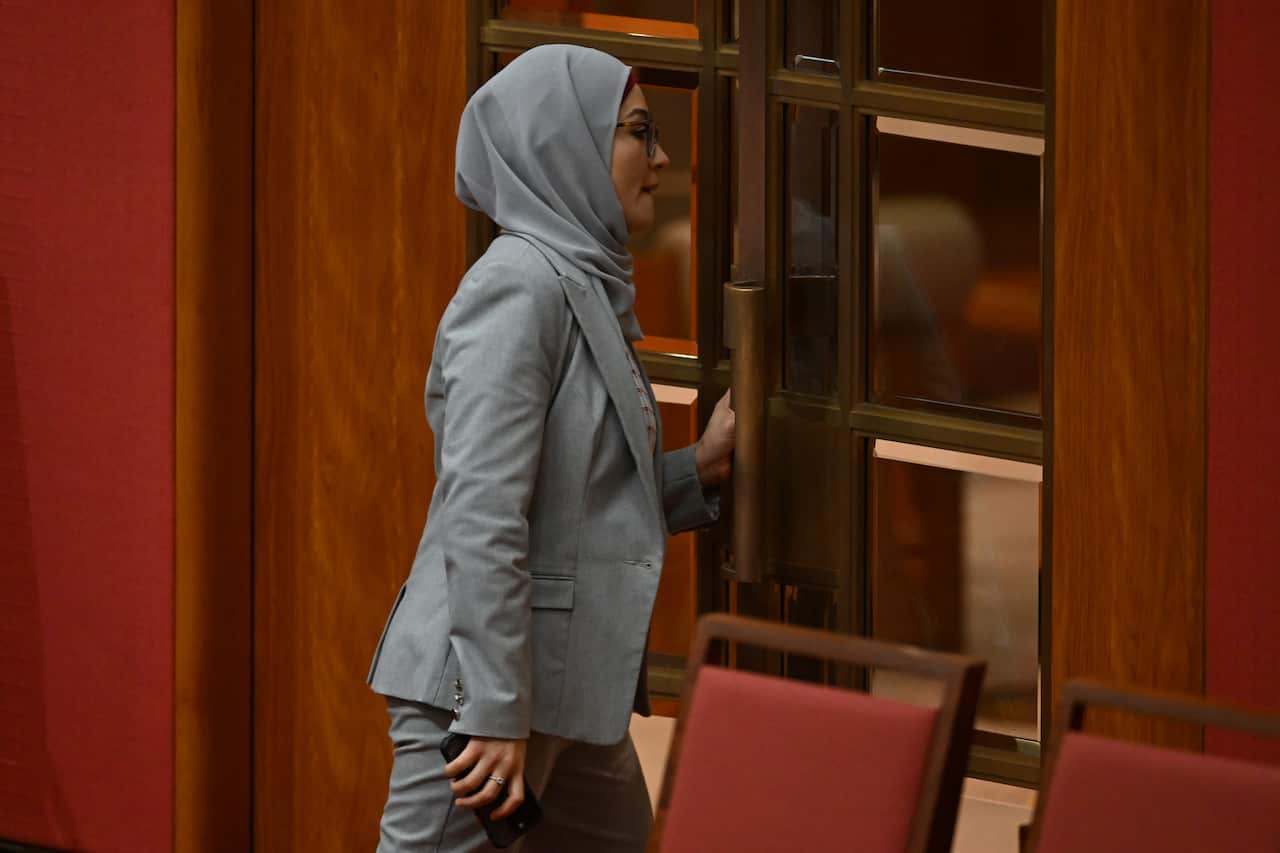 Fatima Payman, in a grey suit and matching scarf, exiting the Senate chamber.