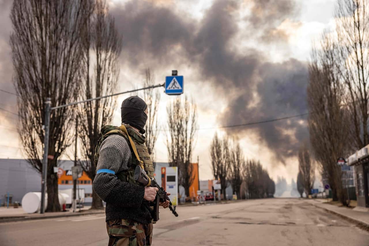 A Ukrainian serviceman stands guard near a burning warehouse.