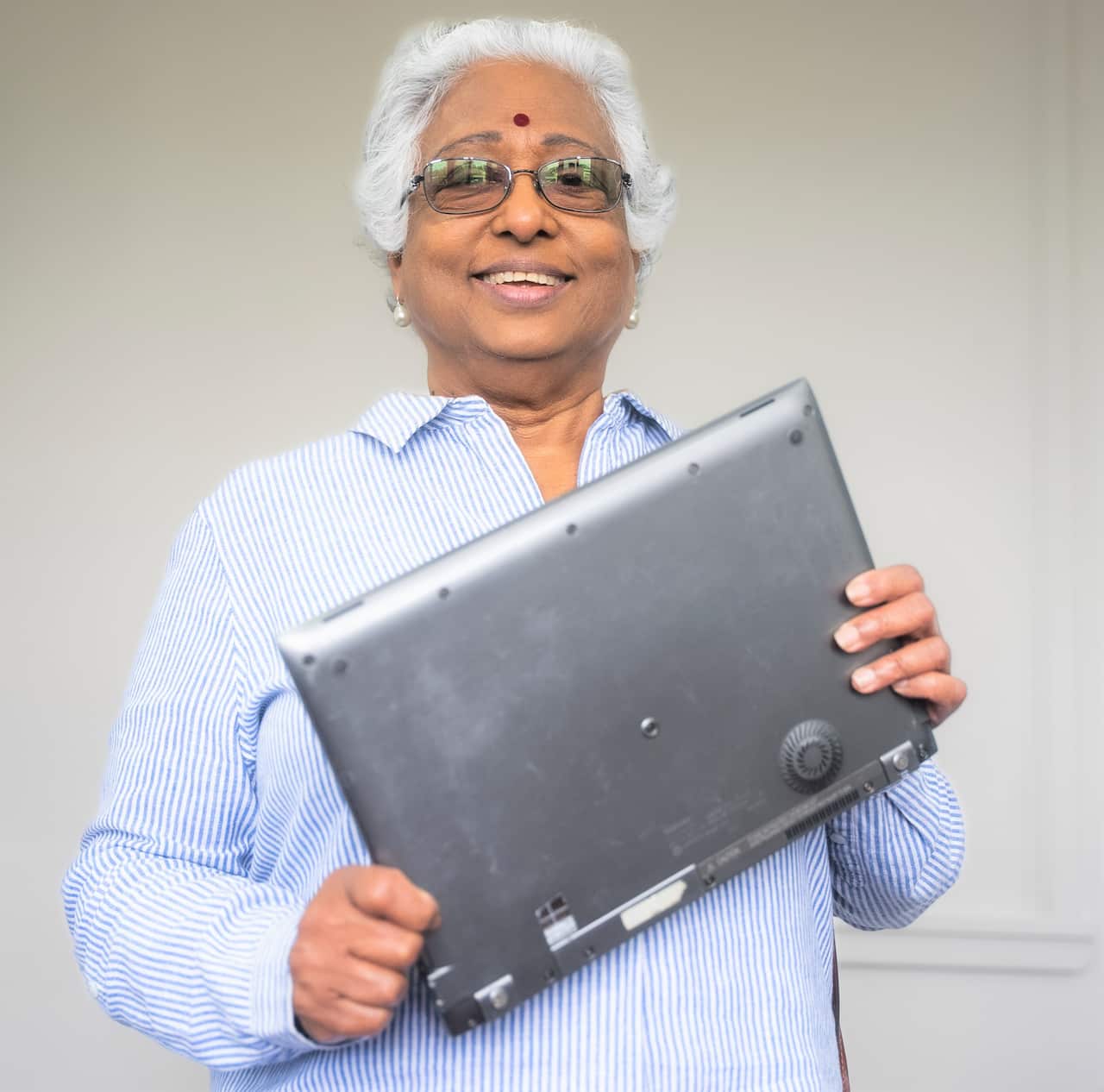 A woman in a blue and white striped shirt holds up a laptop.