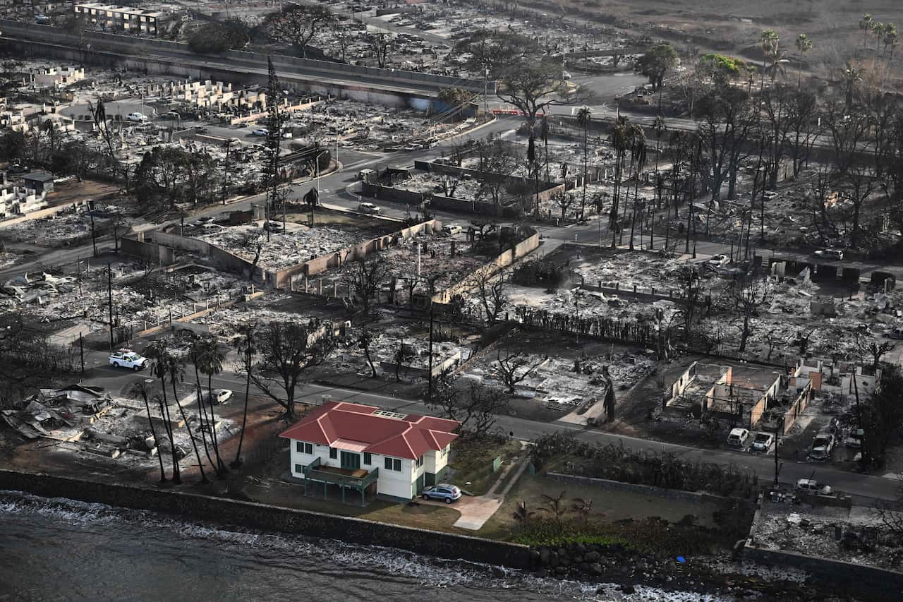 An aerial shot of a devastated area in Maui where only one house, with a red roof, remains.