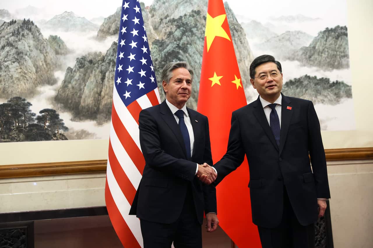 Two men shake hands in front of their respective country's flags.