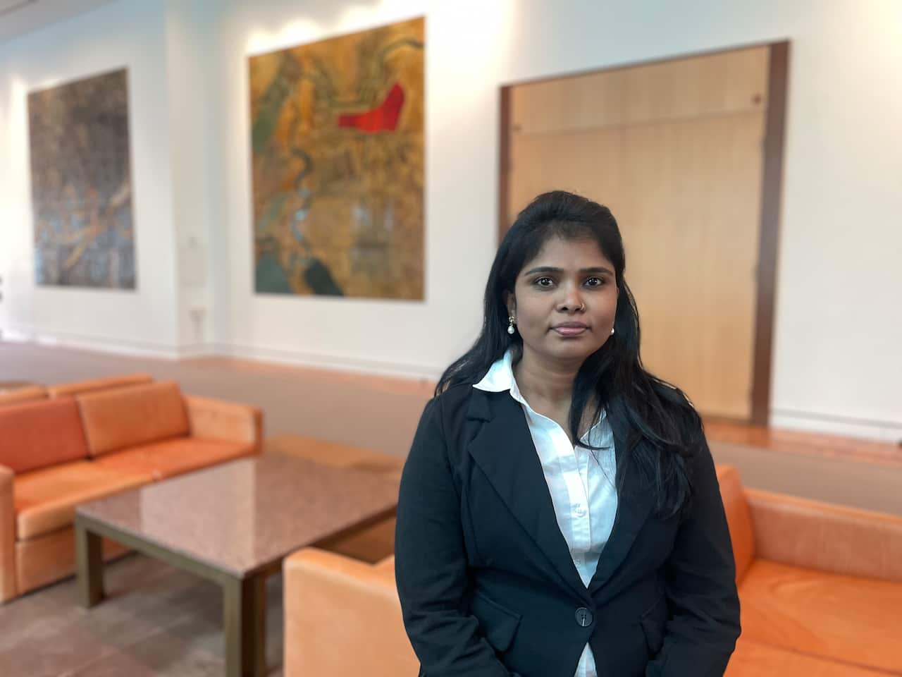 A woman in a black jumper and white shirt standing in a corridor of parliament house