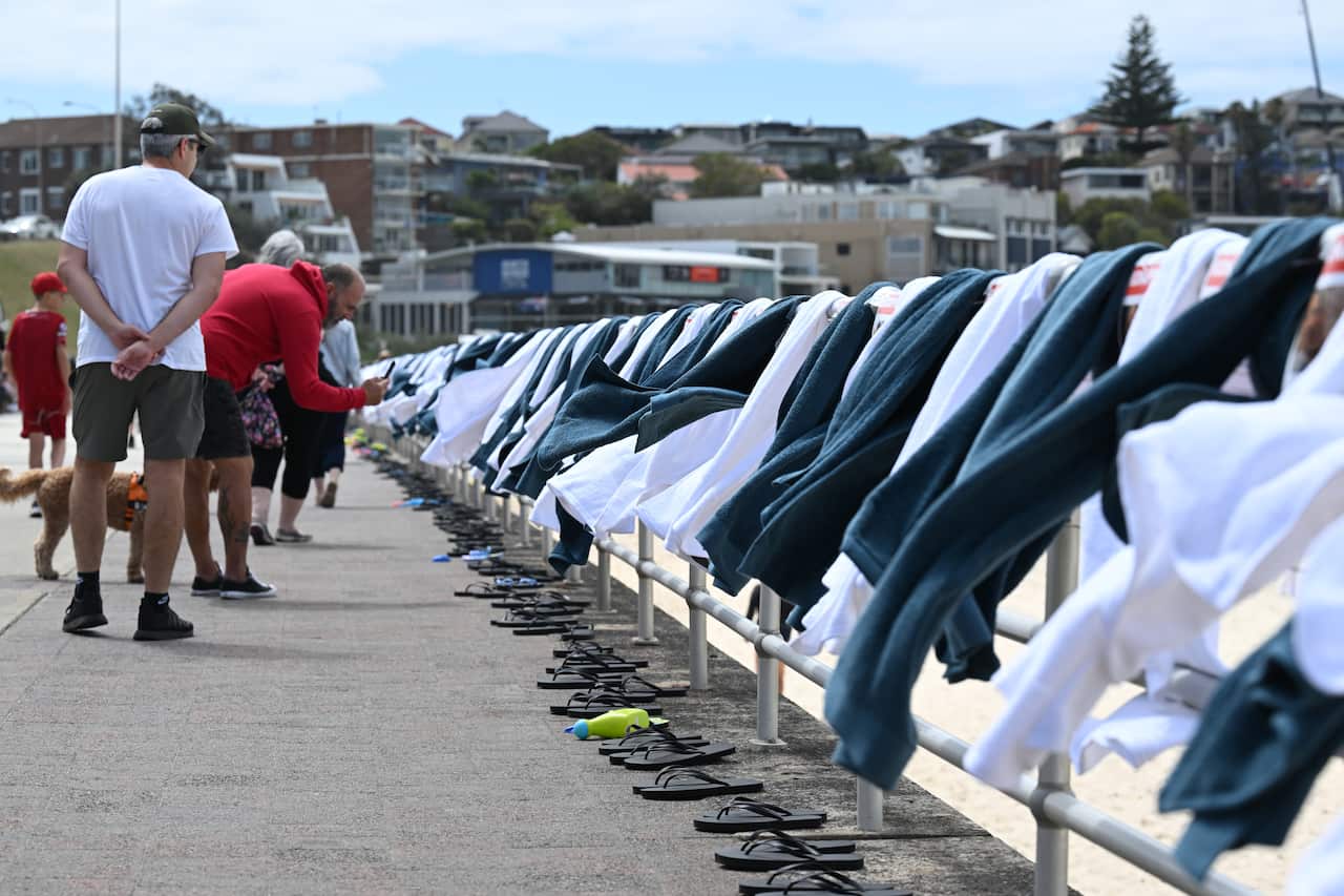 People inspecting a fence at a beach that has towels and posters hung on it.