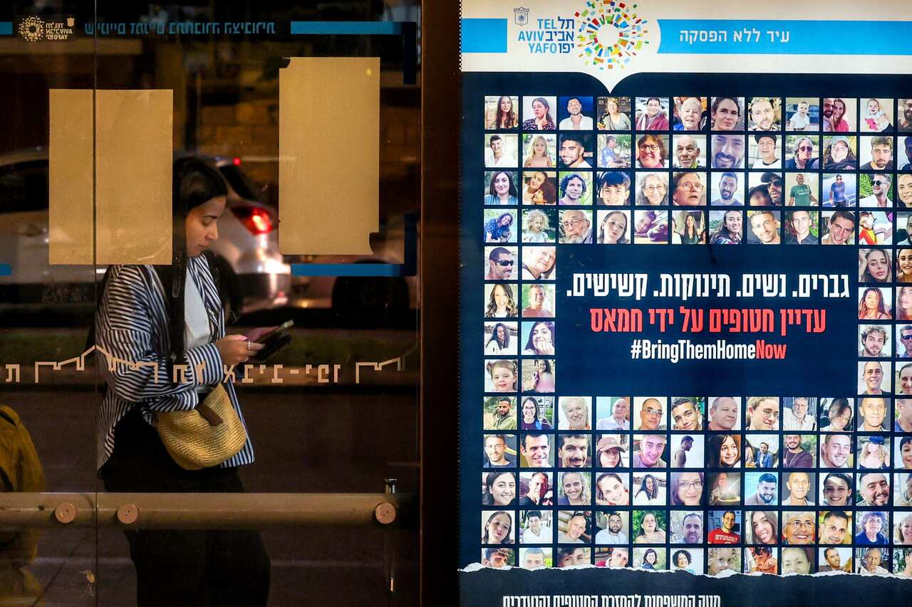 A woman stands at a bus stop in Tel Aviv near a combination of photos and a sign calling for the release of hostages held in the Gaza Strip by Hamas militants.