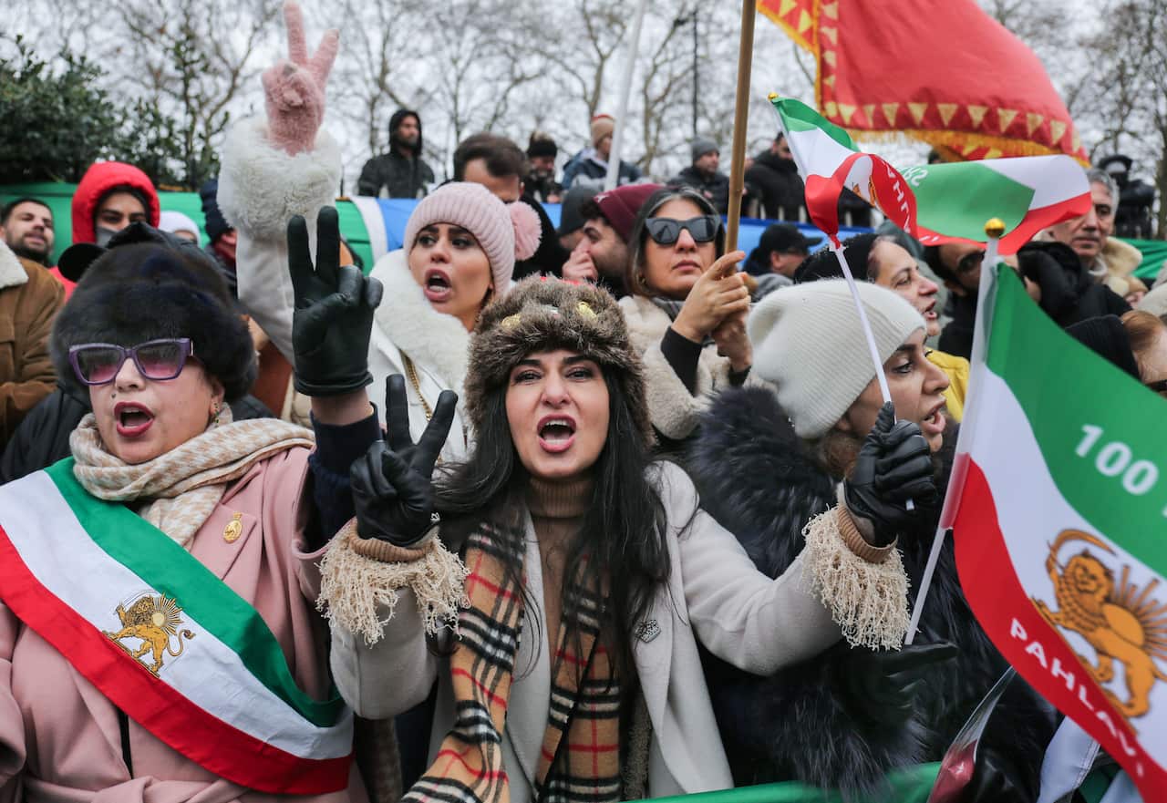 A group of women, some draped in Iranian flags, others holding them during a protest.