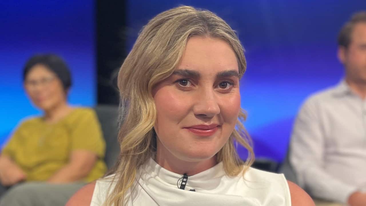 a closeup of a blonde woman in a studio with two blurry people behind her