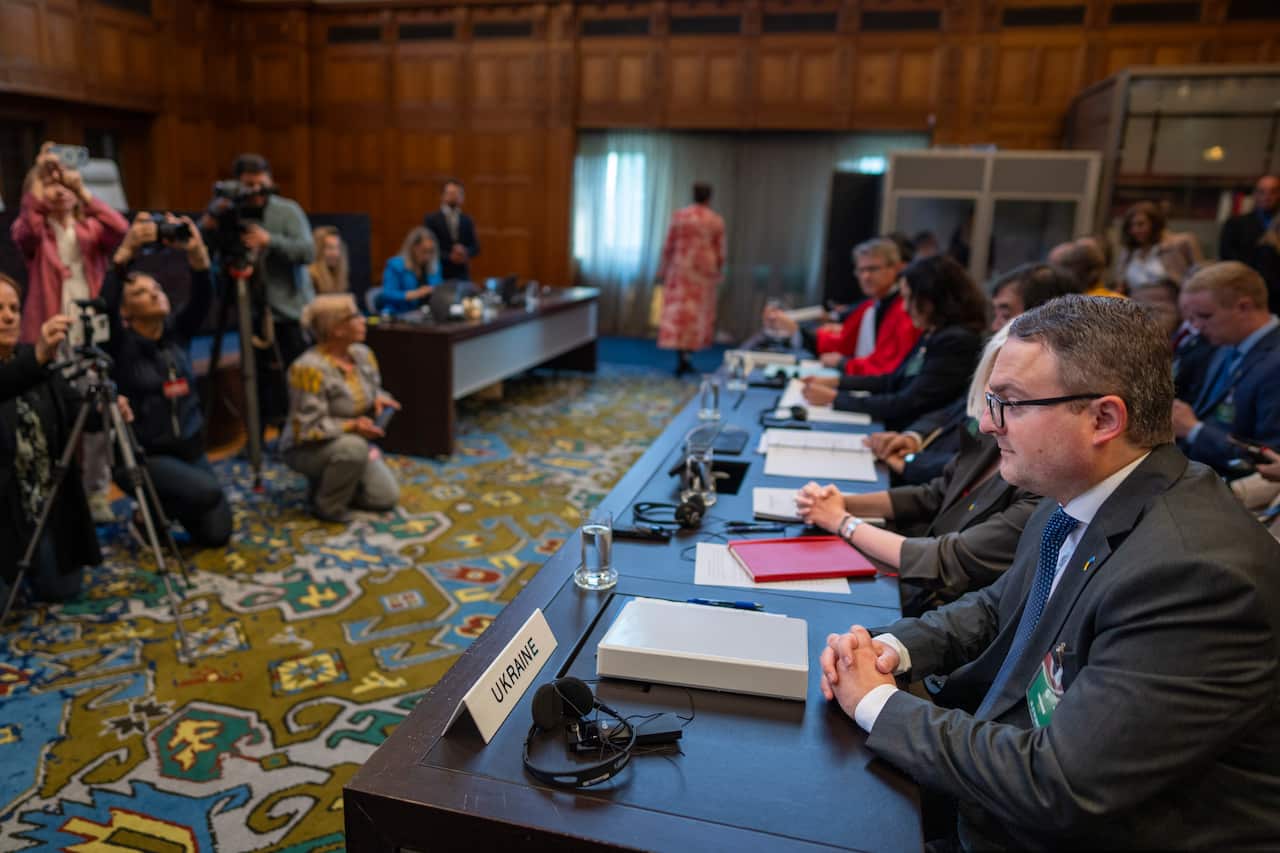 People wearing formal attire sitting at desks in front of photographers.