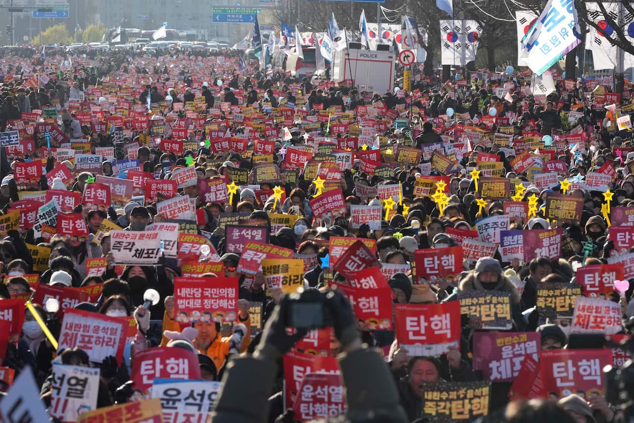 A large crowd of demonstrators holding up white, red and yellow signs written in Korean