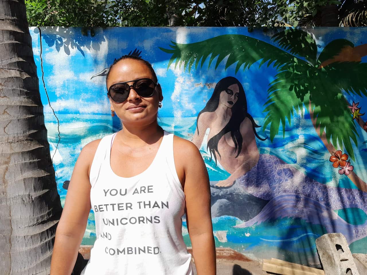 A woman wearing a white singlet and sunglasses standing outside