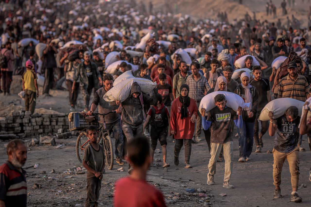 Hundreds of people walking along a pathway, carrying white sacks.