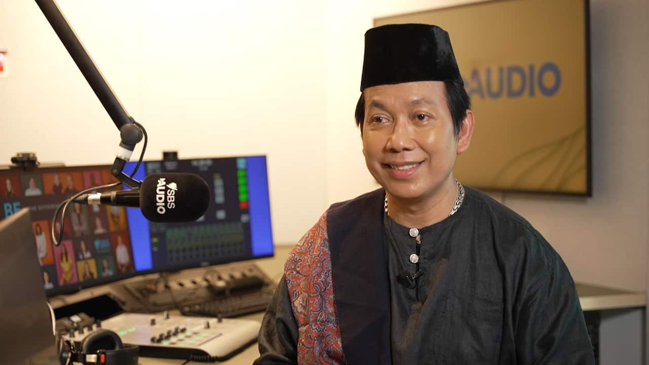 A journalist sitting in a studio. In front of him is a microphone that says "SBS Audio".