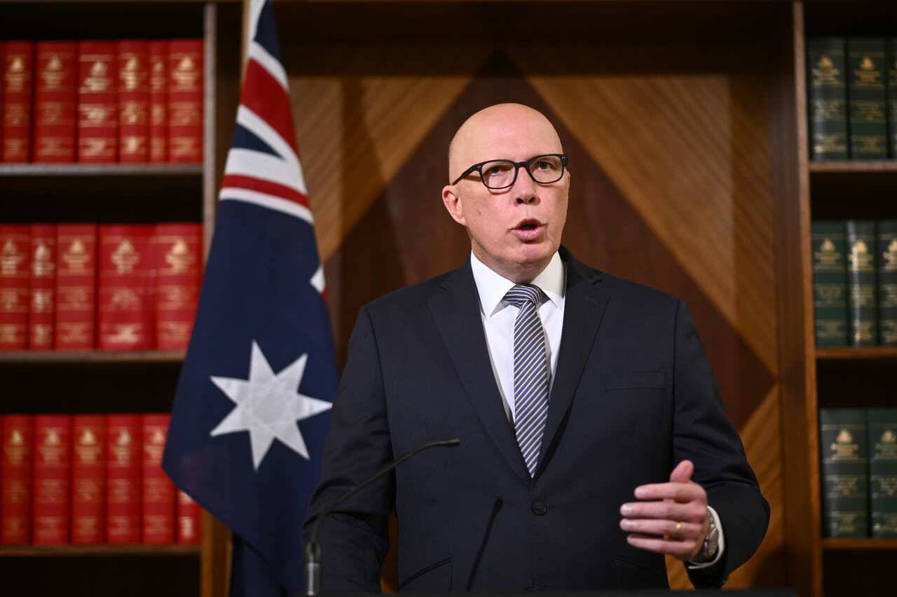A man in a suit speaks in front of the Australian national flag during a press conference.