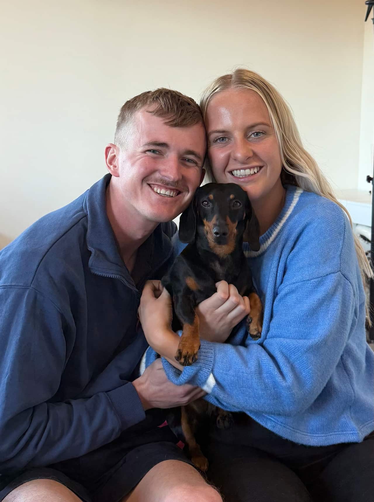 Two people smiling while holding a small dog.