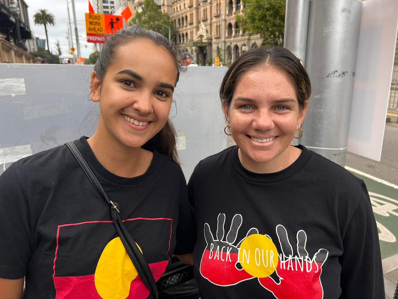 two young women smiling, both women t shirt with aboriginal flag colours