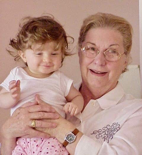 An elderly woman holding a small child in her hands. They are both smiling.
