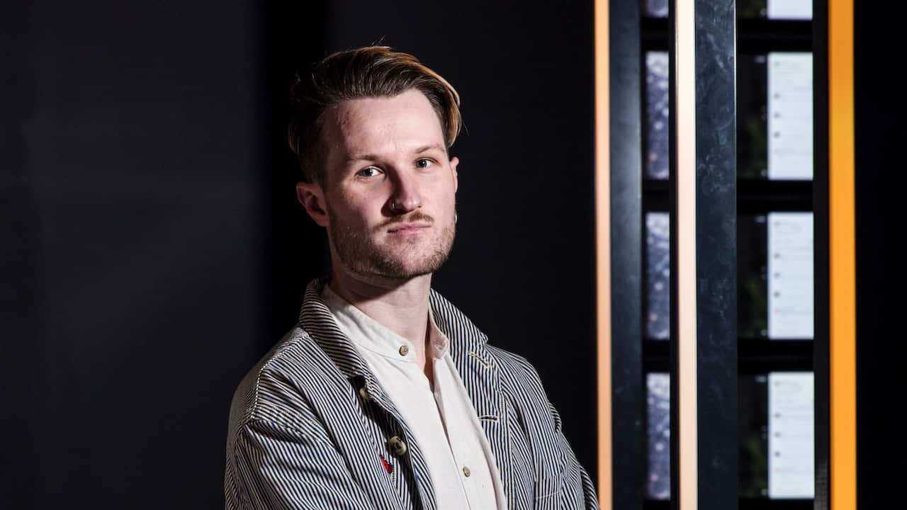 A man with short brown hair, wearing a white shirt and pinstripe jacket. He's staring at the camera.