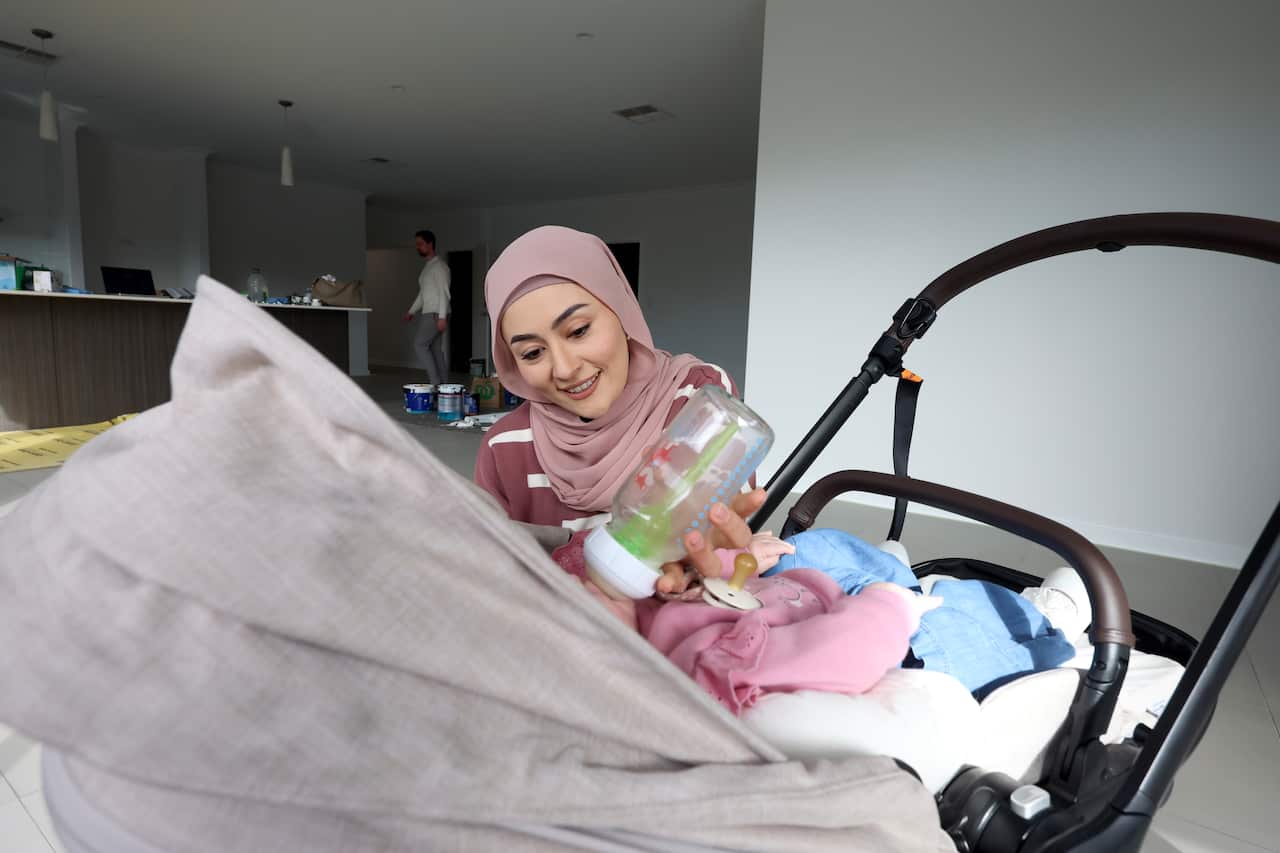 Fatima Payman feeds a bottle to her daughter, who lies in a stroller in a family room.