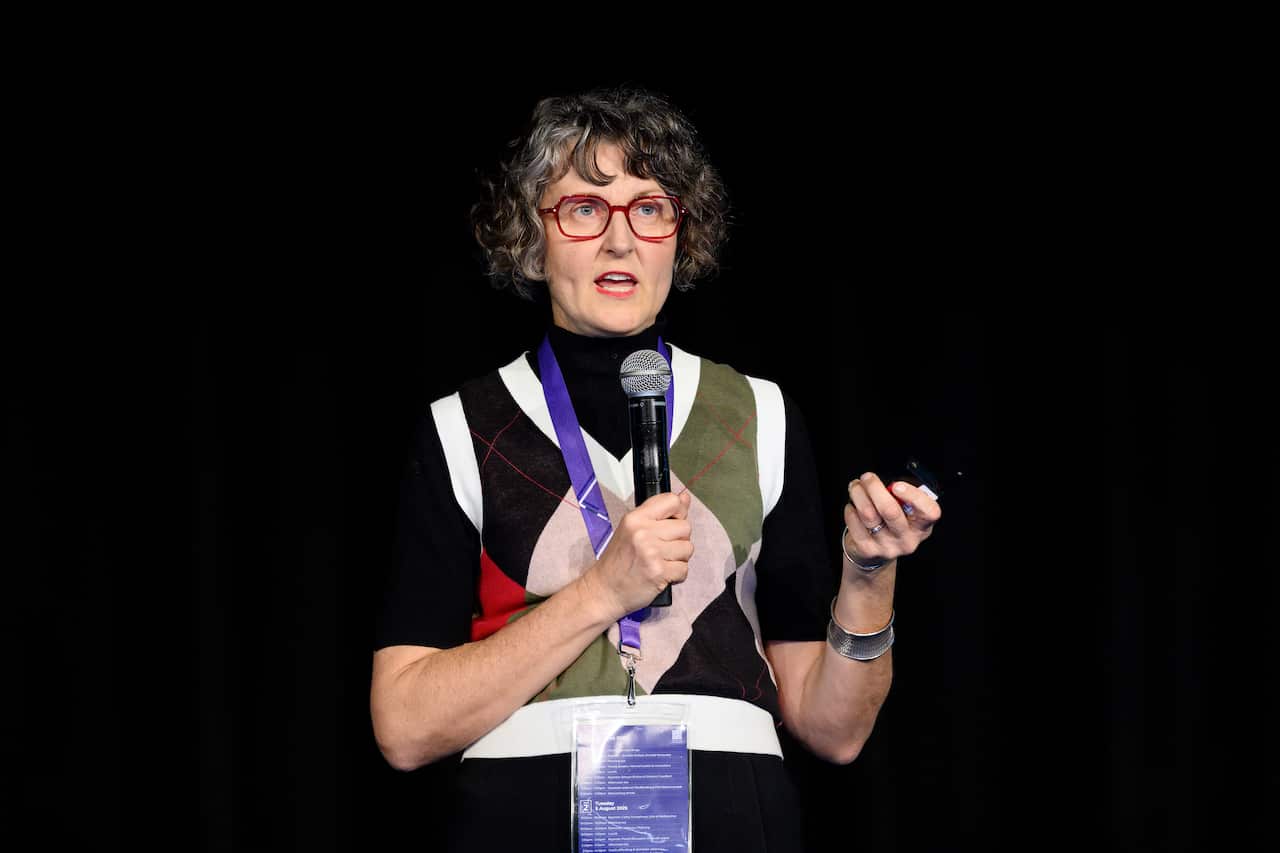 A woman wearing a colourful vest speaking into a microphone she's holding.