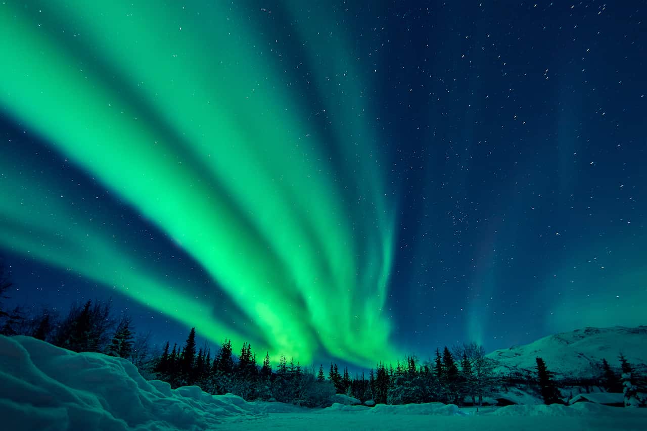 Green lights of the Aurora Borealis in the sky over a frozen landscape.