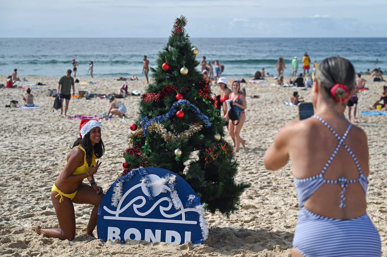 People take photos with a Christmas tree on a beach.