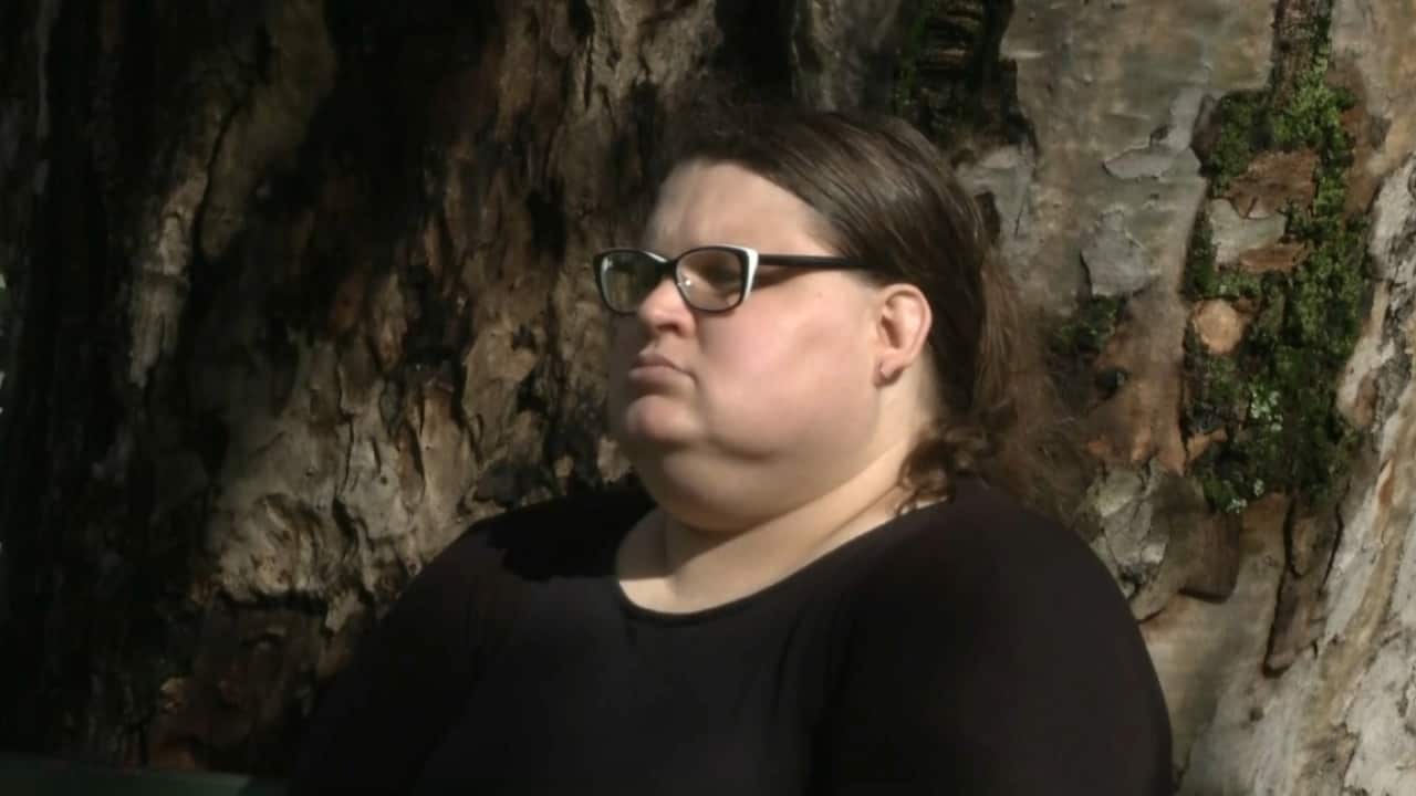 A woman wearing glasses and a dark top standing next to a tree