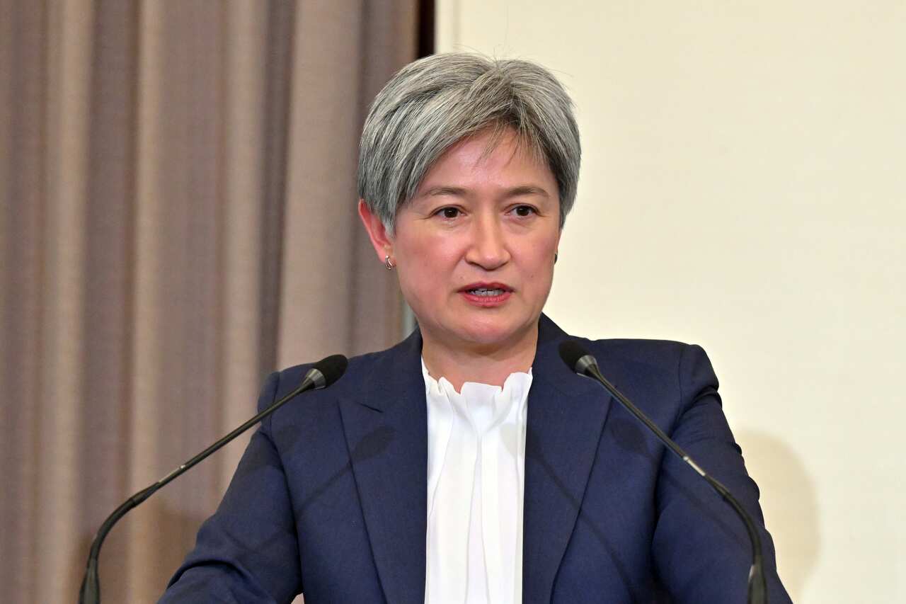 A woman wearing a blue blazer and white shirt speaking into a microphone.