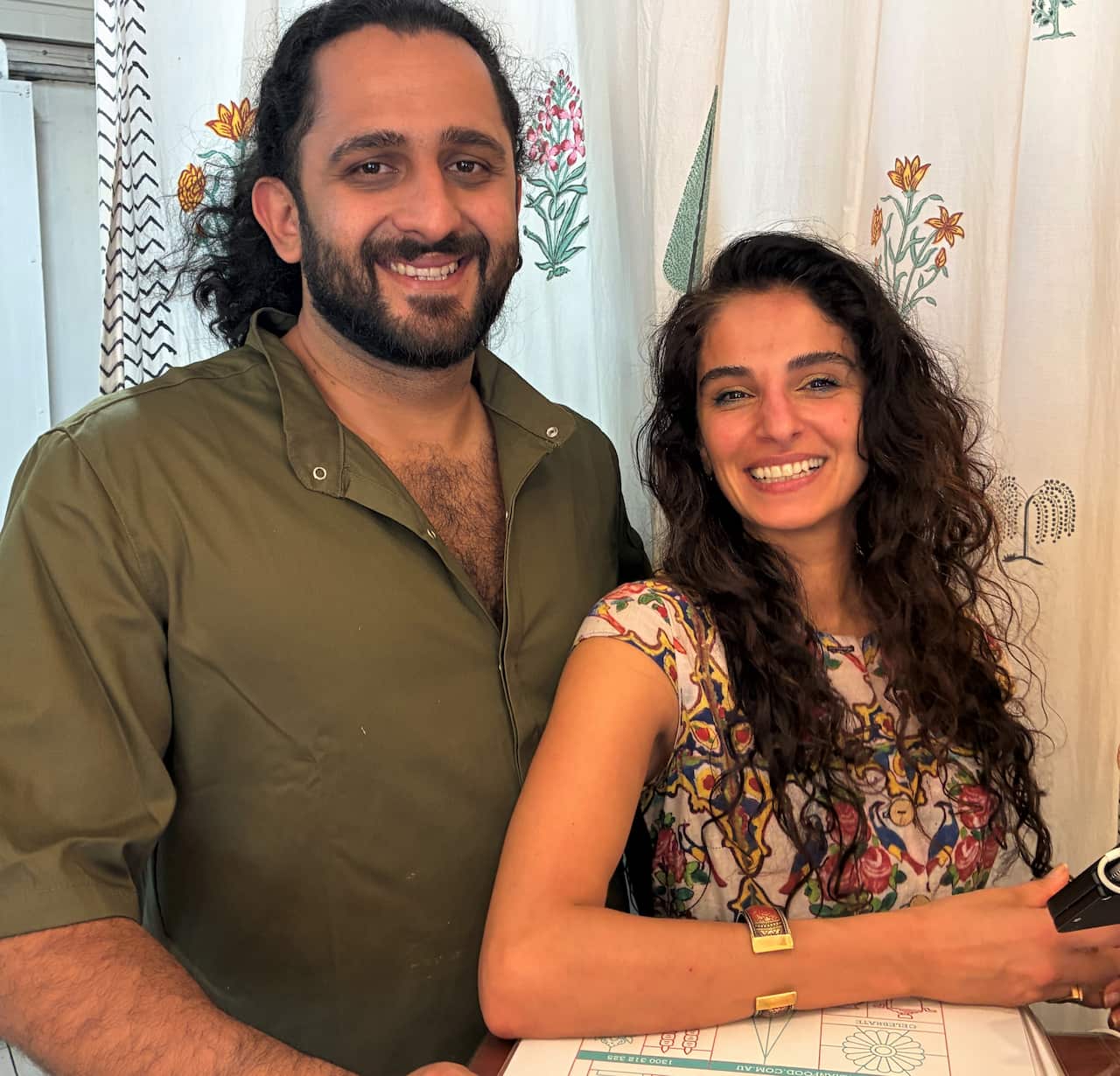 A man with a beard wearing a green shirt stands next to a woman with long brown hair. 