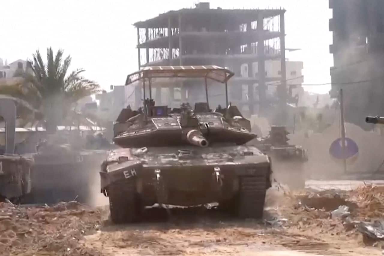 A tank being driven through the streets of a city.