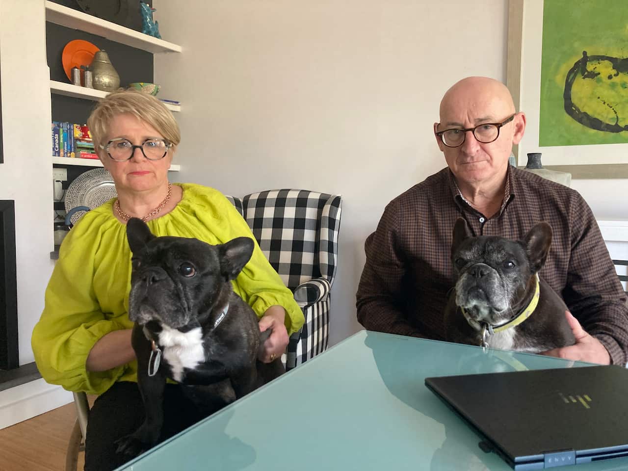 A man and a woman sitting at a table with a dog in each of their laps 