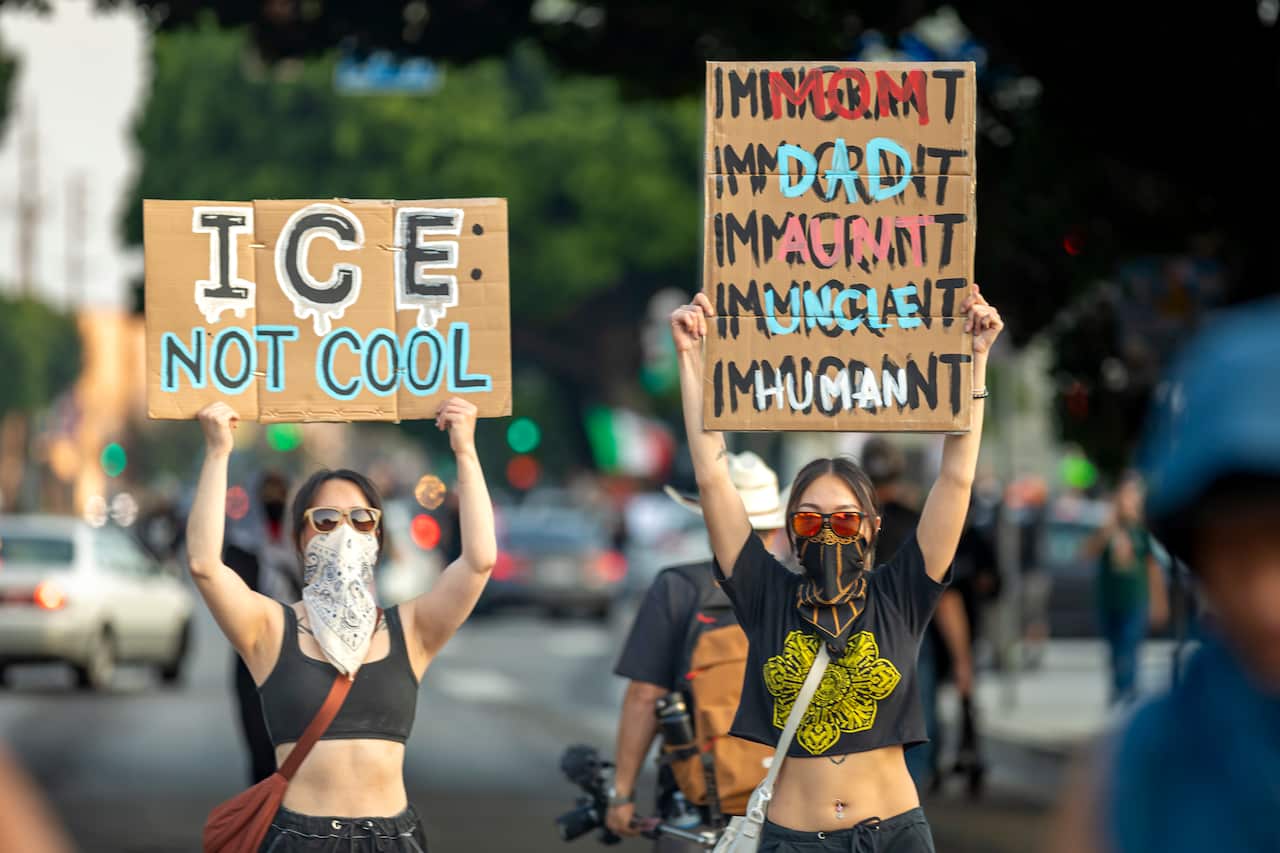 Two women holding up signs during a protest. One sign reads: "ICE: Not cool", the other reads "dad, aunt, uncle, human over the words "innocent".